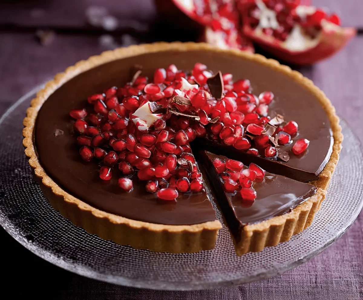 Delicious Chocolate Pomegranate Tart topped with fresh pomegranate seeds and a glossy chocolate glaze on a white plate