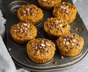 Delicious homemade pumpkin almond flour muffins on a white plate with fresh pumpkin and almonds in the background
