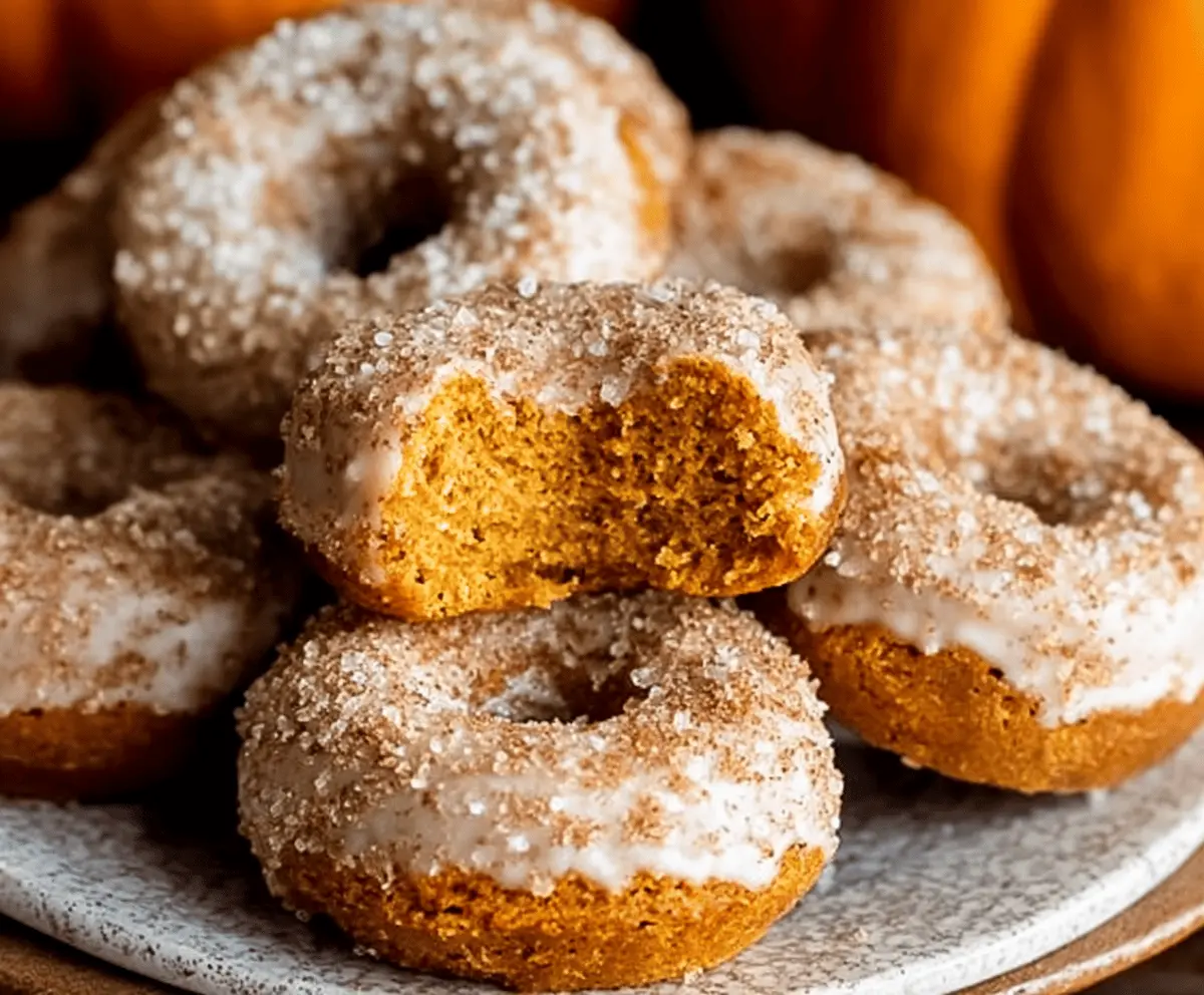 Freshly baked pumpkin donuts topped with cinnamon and powdered sugar on a rustic plate, perfect for fall treats.